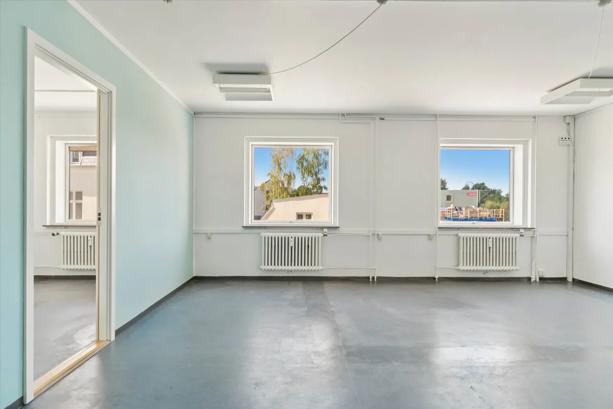 Lejlighed med to vinduer og hvide vægge og loft samt hvide radiatorer og lysegul væg på den ene side