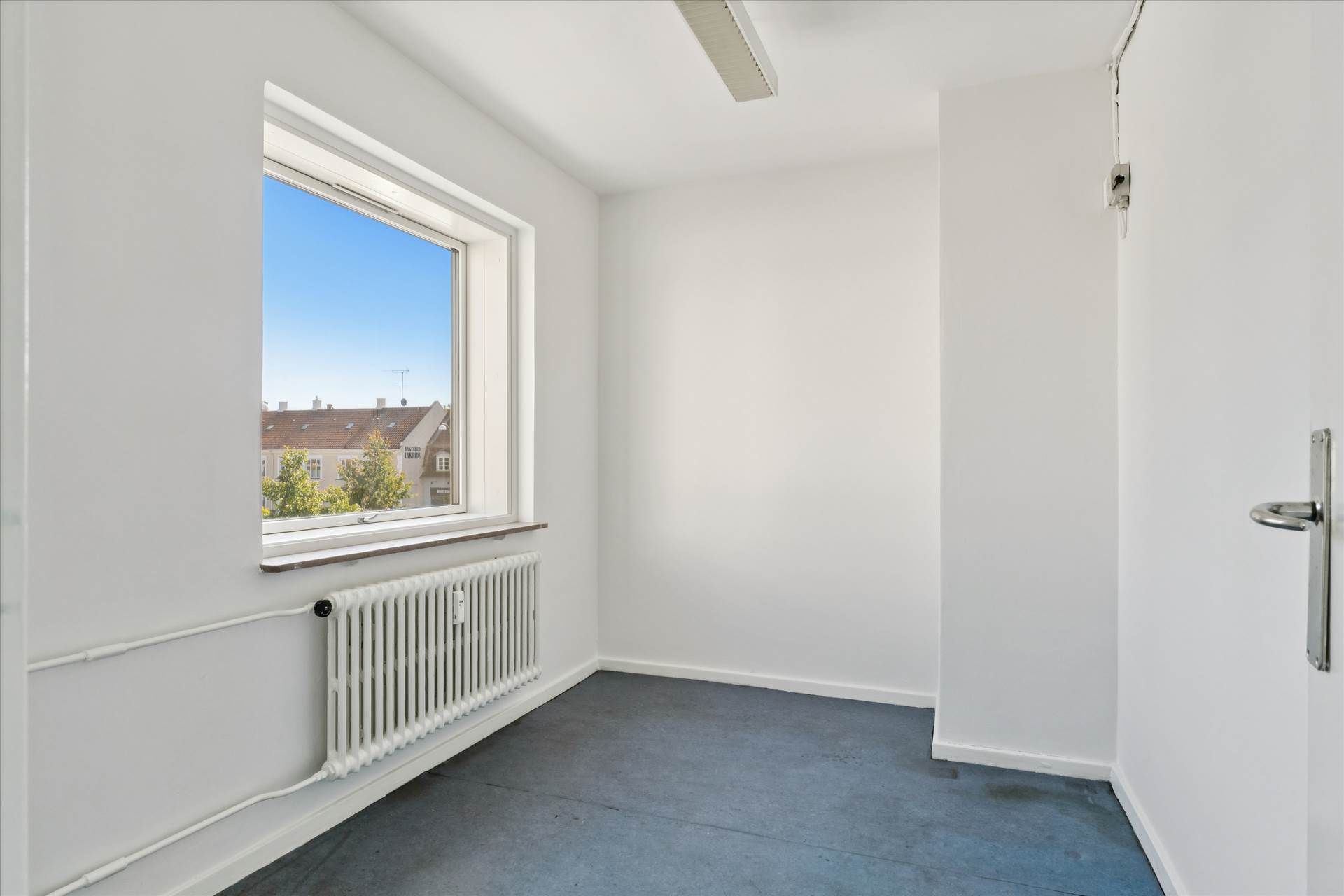 Lejlighed med lyse og fleksible rammer og et vindue med udsigt til bygninger og træer i baggrunden