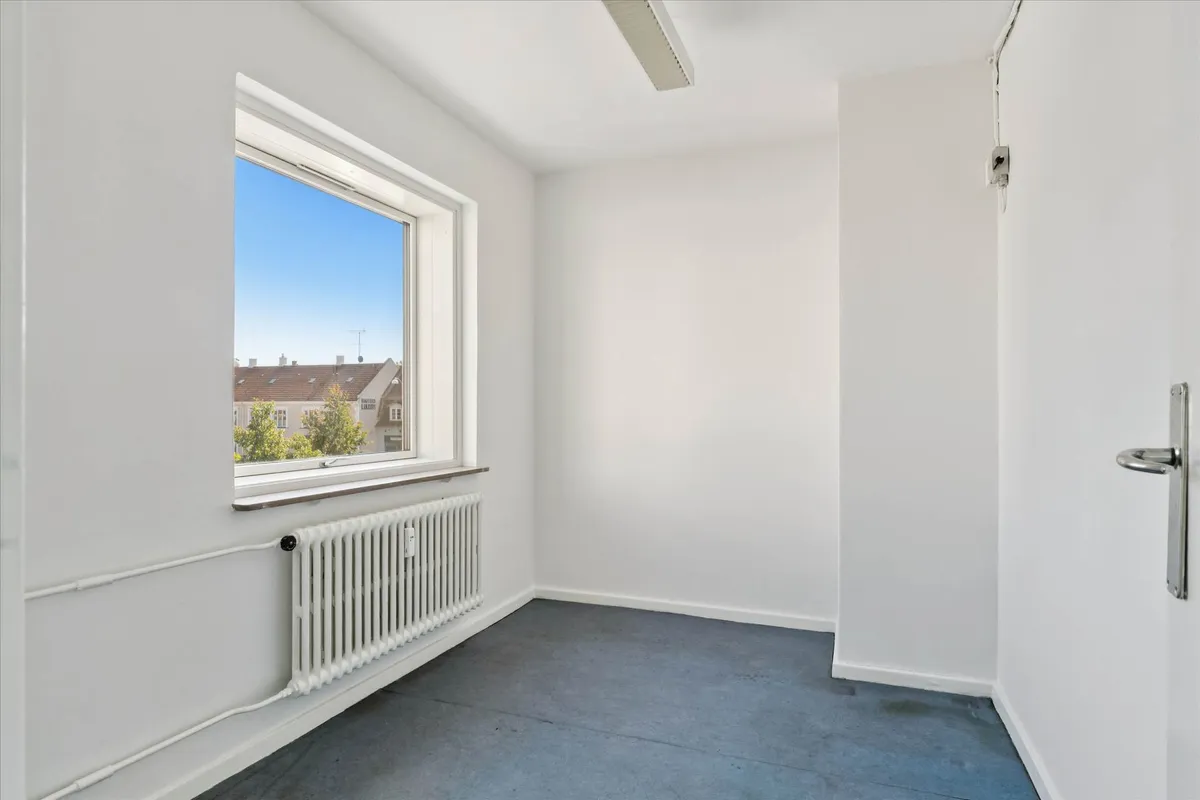 Lejlighed med lyse og fleksible rammer og et vindue med udsigt til bygninger og træer i baggrunden