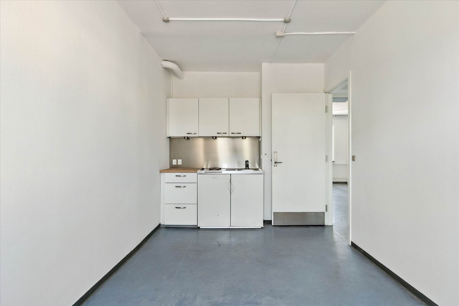 Lys og ren stue med hvide vægge og loft samt gulv, køkken med brædder, strygejern og køleskab samt lysekroner og åbne døre