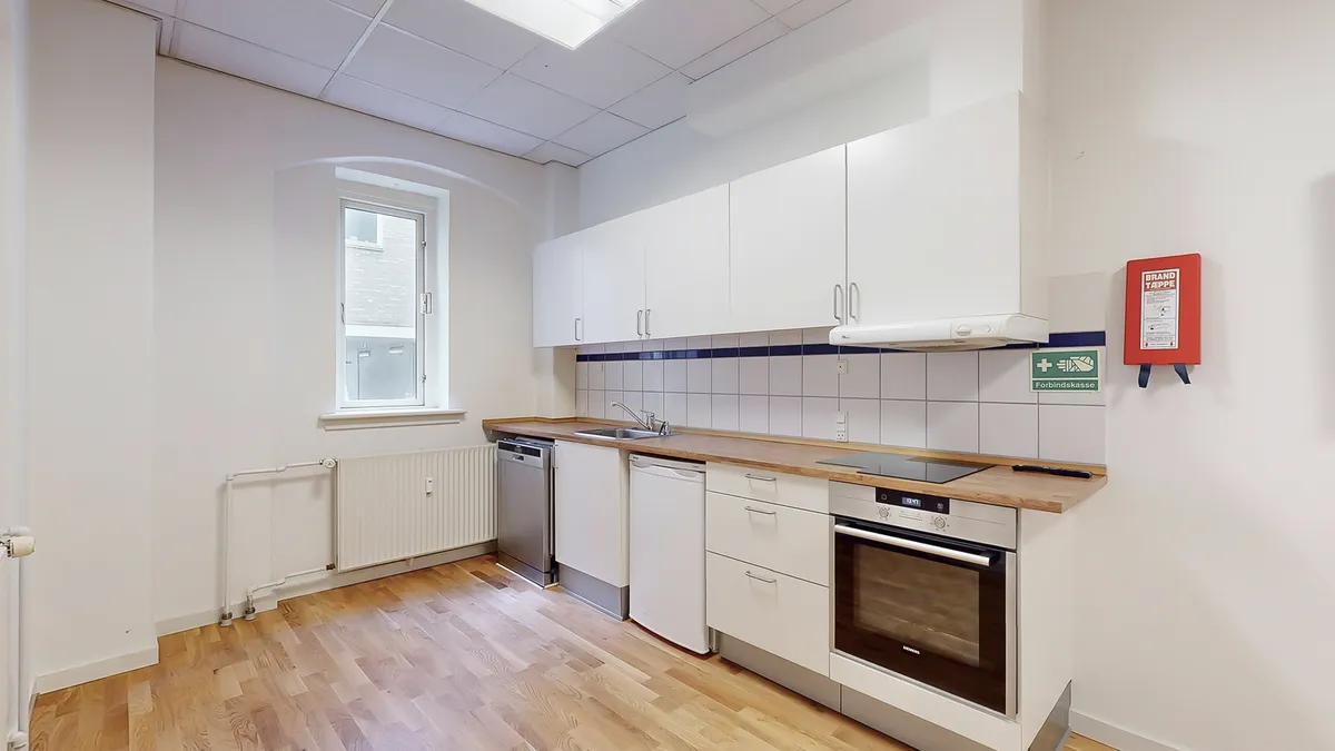 En moderne, hvidt indrettet køkken med lyse trægulve, lysegrå vægge og hvide møbler og apparater