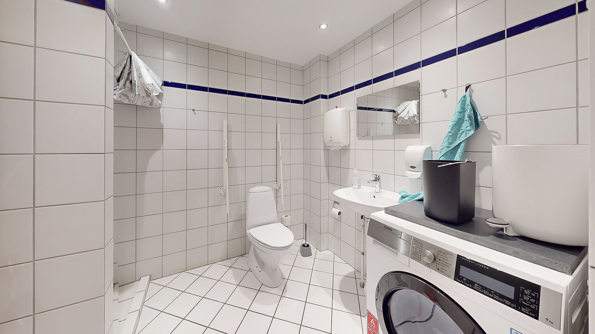 Rent og velholdt badeværelse med toilet, håndvask og vaskemaskine i reneste hvidt og blåt