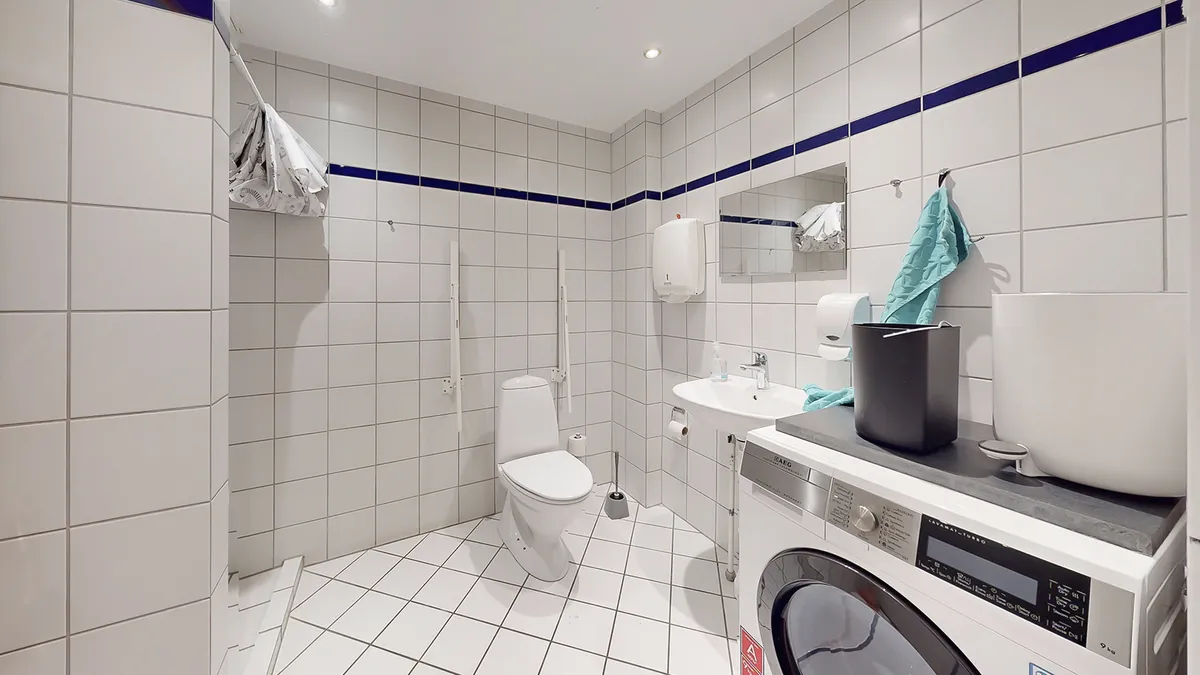 Rent og velholdt badeværelse med toilet, håndvask og vaskemaskine i reneste hvidt og blåt