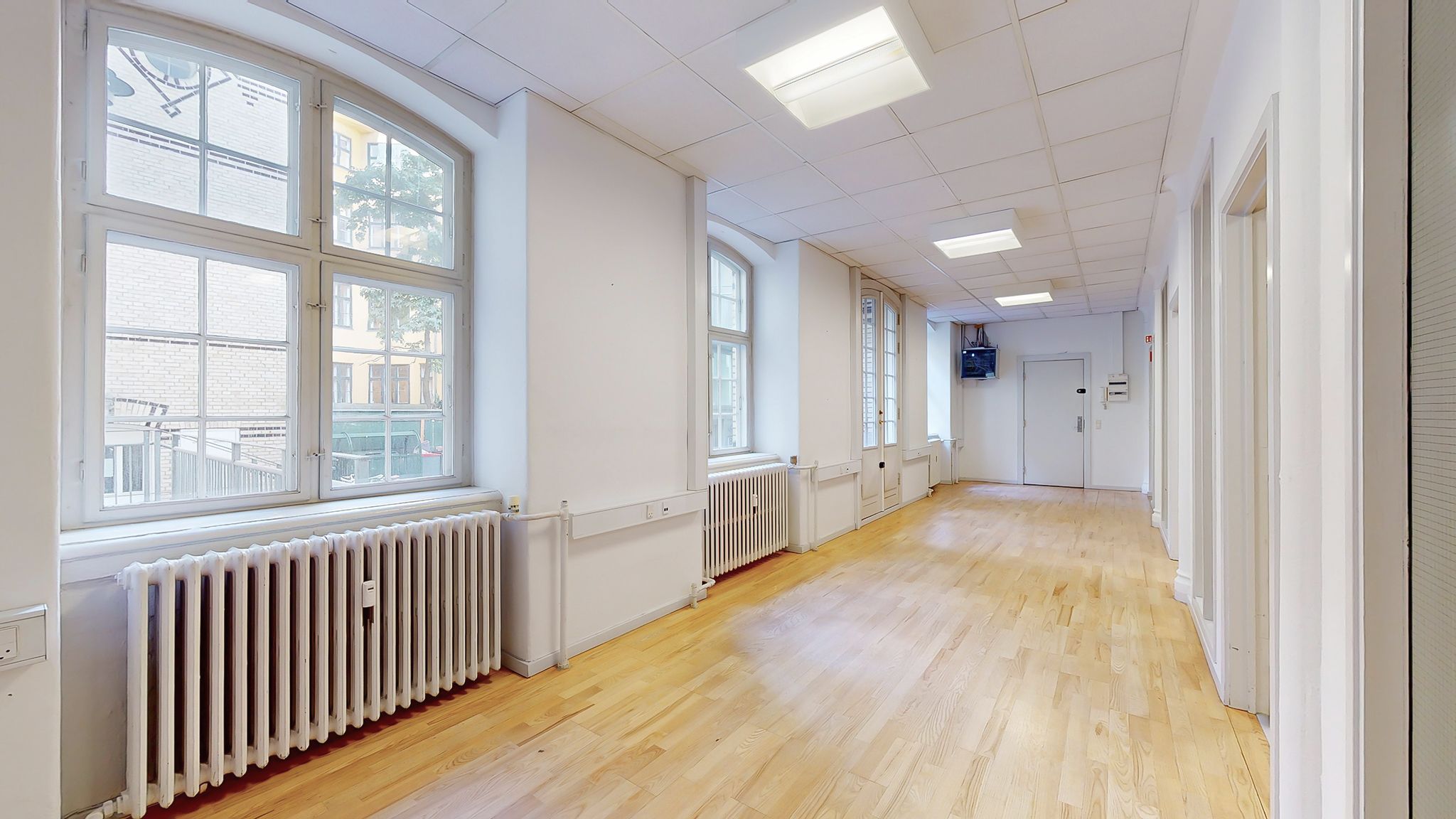 Kort og lyst kontor med hvide vægge og lyse gulve samt store vinduer med udsigt til bygninger i baggrunden