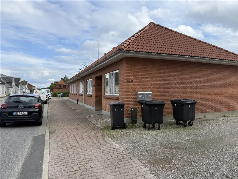 Udlejningsejendom i Taulov med røde mursten og hvide ruder, to hjulde trommer og to hjulde kubikter placeret på en