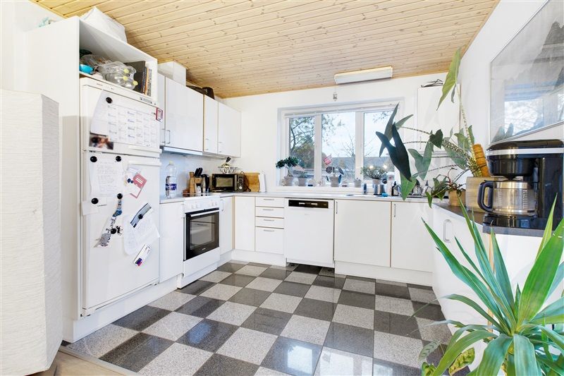 Et moderne køkken med hvide vægge og loft, en hvid køleskab og ovn, og en møbleret spiseplads med krydsfinergulv