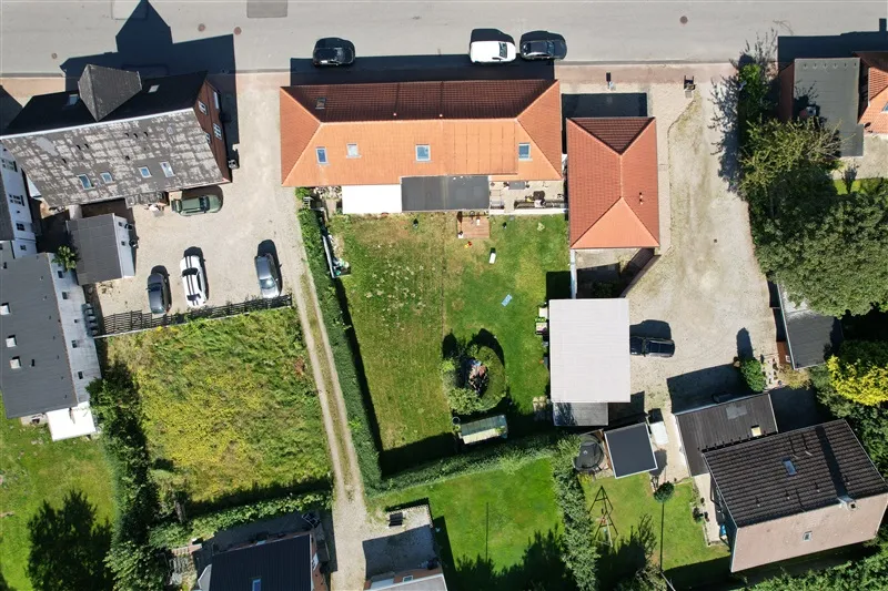 Forskellige huse med parkeringspladser og haver i Taulov, med en større grøn græsplæne og et hvidt hus i baggrunden