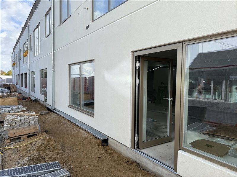 Et nybygget erhvervslokale i Middelfart med åbne glasruder og vinduer og jordpakker og jordlæsser til siden