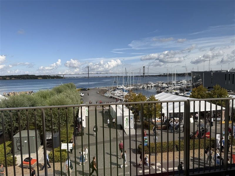 Et stort udendørsområde med flere mennesker, hvor nogle går og står, mens andre er på en bådhavn med mange både og telte