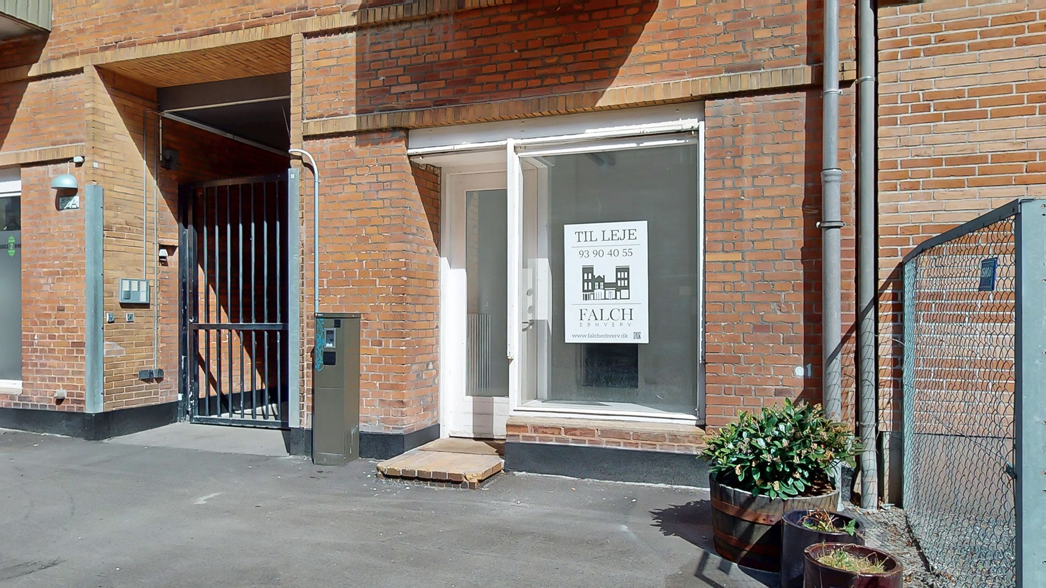 Lejlighed med glasdør og skilt med teksten Til Leje. På skiltet er der en logo og et telefonnummer. Der er en port i