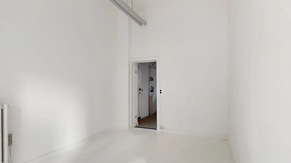 To hvide vægge, hvor en dør er åben, og der er en lampe, der hænger fra loftet, samt en radiator og en stikkontakt på højre