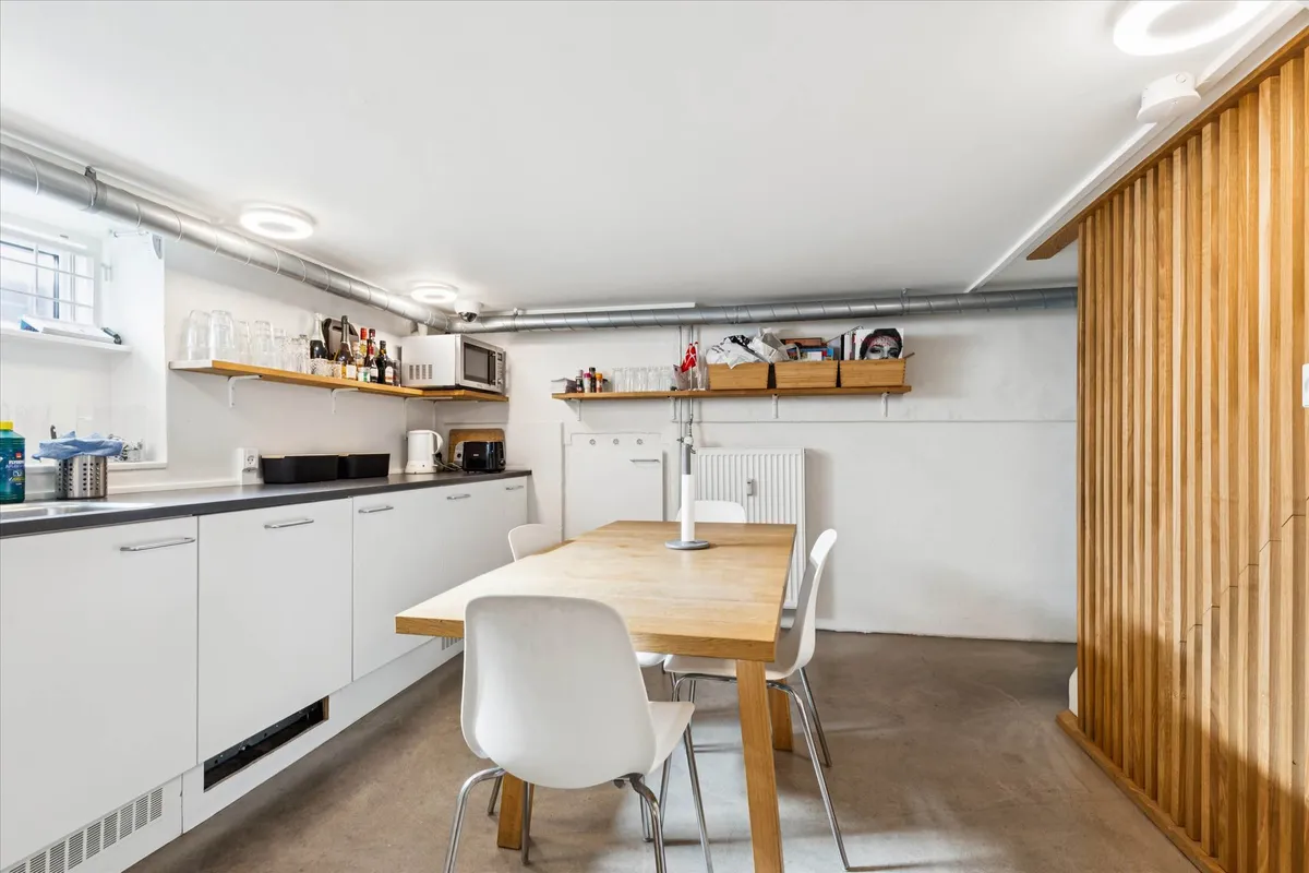 Minimalistisk køkken med hvide vægge, massiv træspisebord og hvide stole, små højre og et mikroovn samt en række glas og