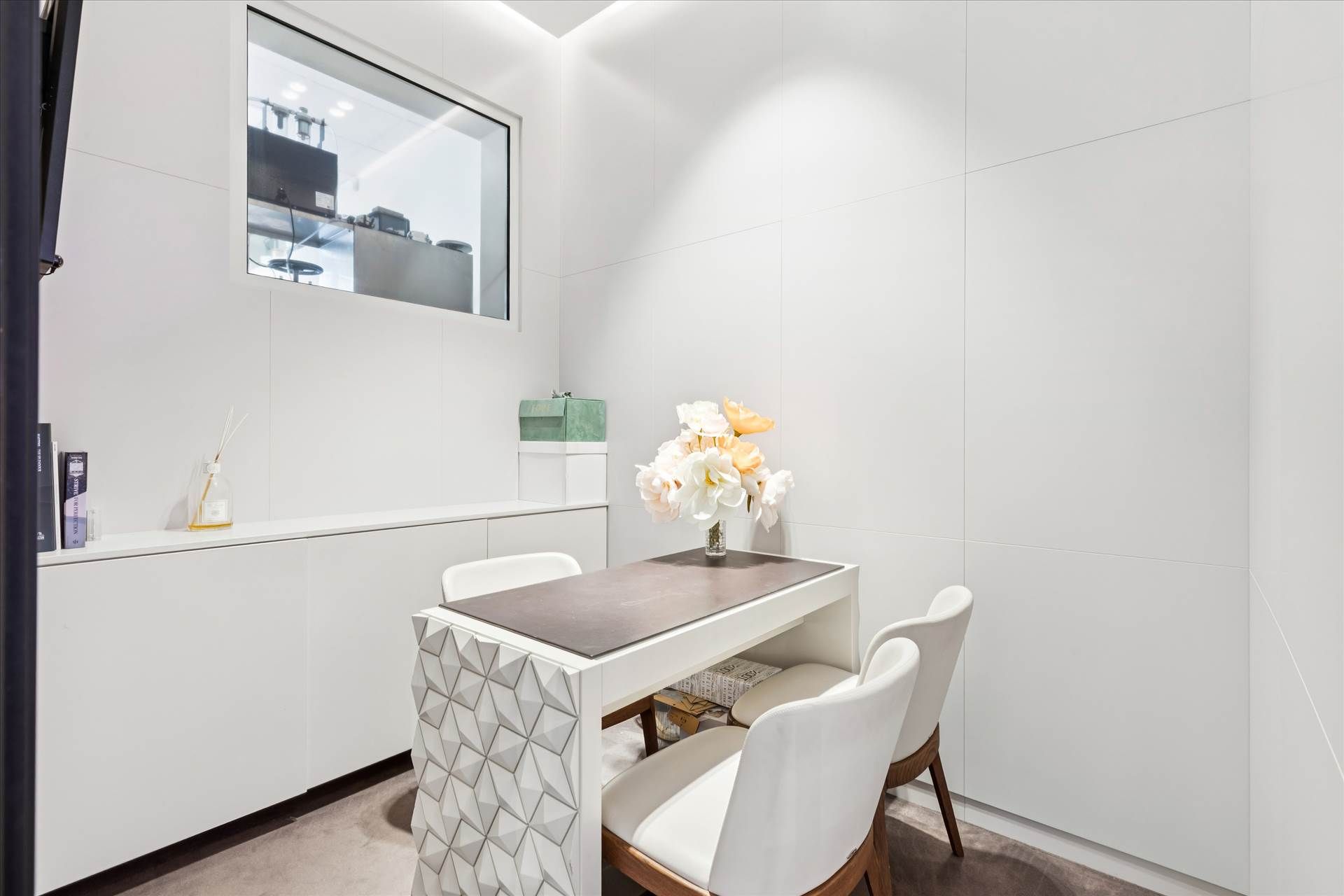 Et luksuriøst og rent kontor med en hvid væg og en hvid bord med blomster i en vase og et sæt hvide stole med brændte sæder