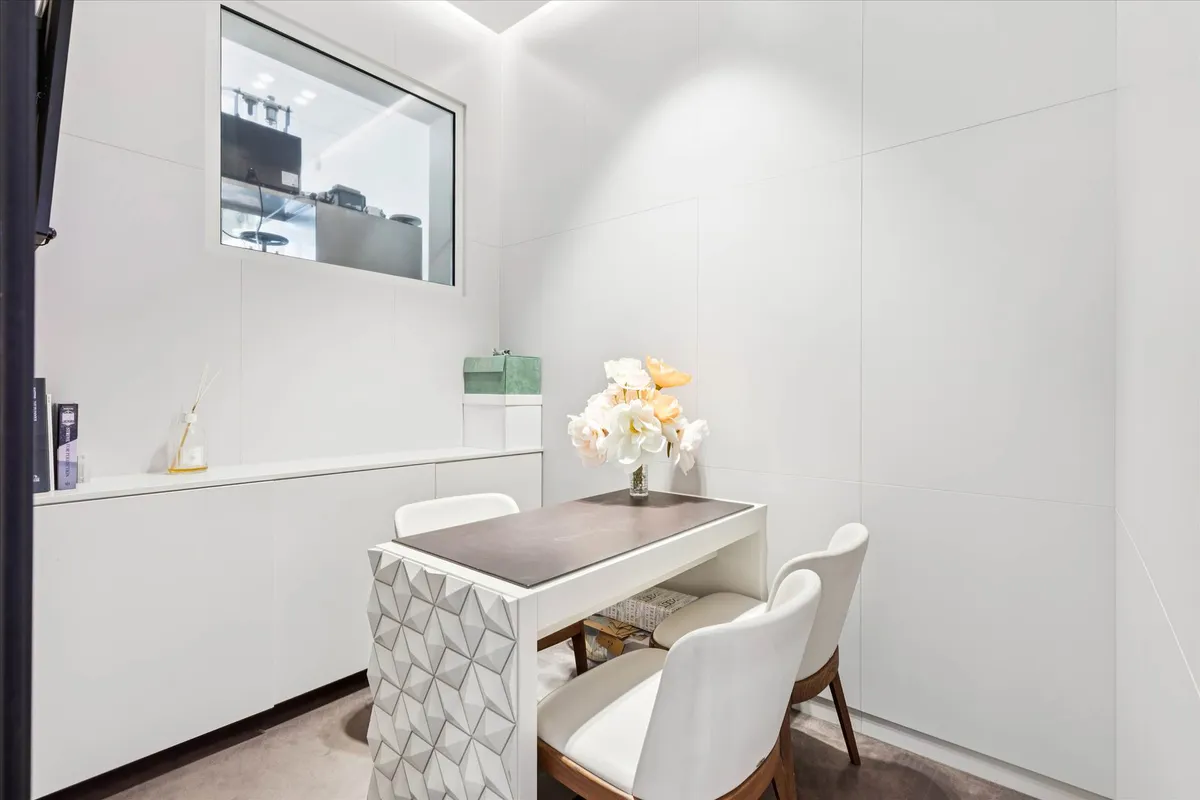 Et luksuriøst og rent kontor med en hvid væg og en hvid bord med blomster i en vase og et sæt hvide stole med brændte sæder