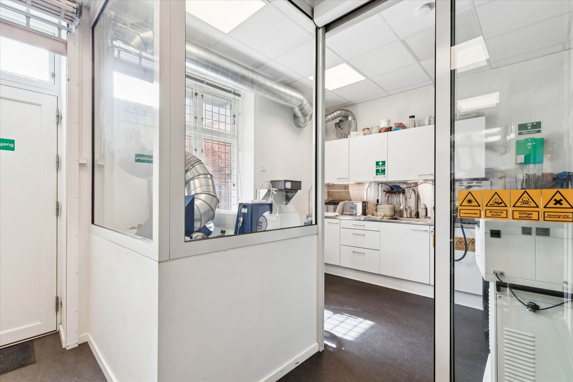 Laboratorium med flere apparater og højtryksblæser. Hvid indretning og glasdøre. Farvede skilte og højtryksblæser