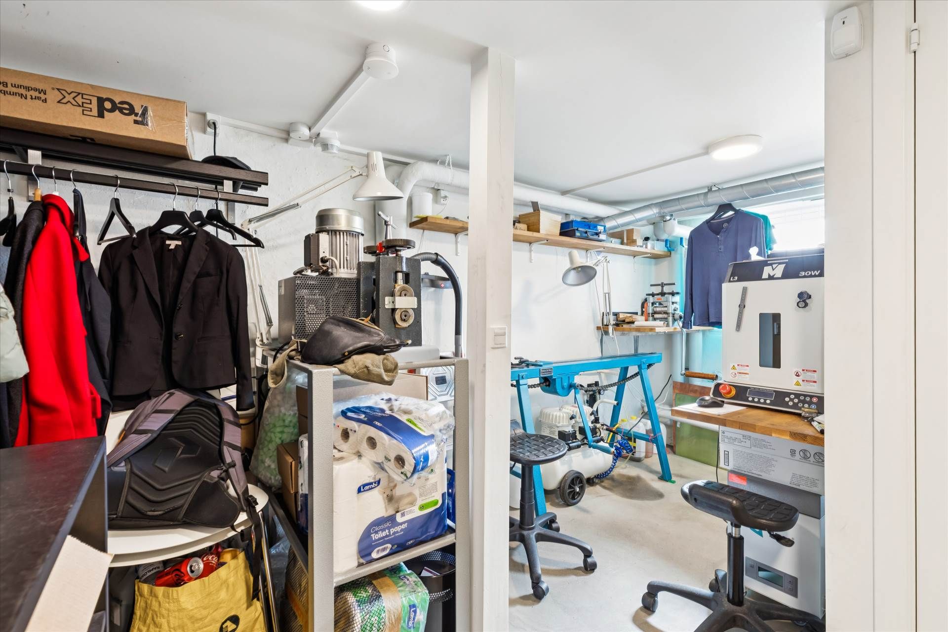 Et værksted med værktøj og materialer, hvor der er en maskine og en lampe på et bord samt en stol og en arbejdstol.