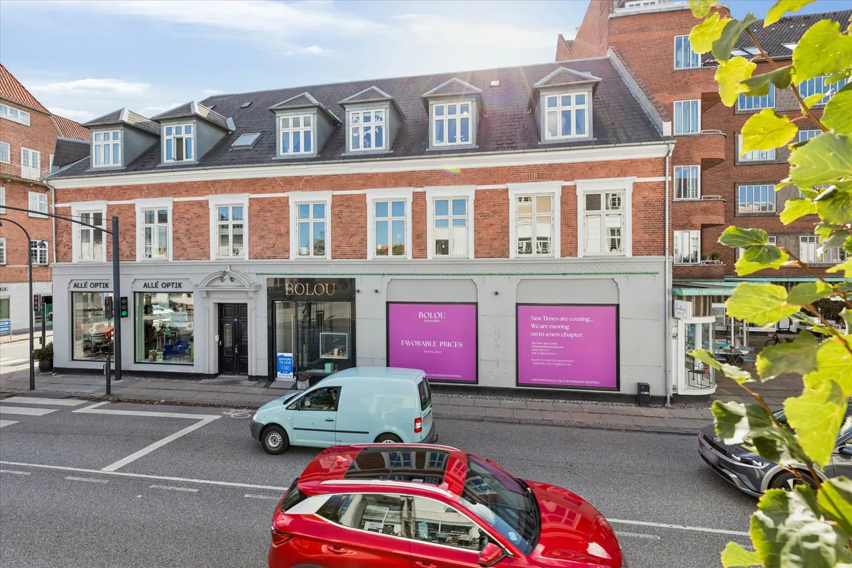 På Jægersborg Allé, er der en rødmalet bygning med hvide vindueskarme og facader, hvor der er skilte med navnene Alle Optik