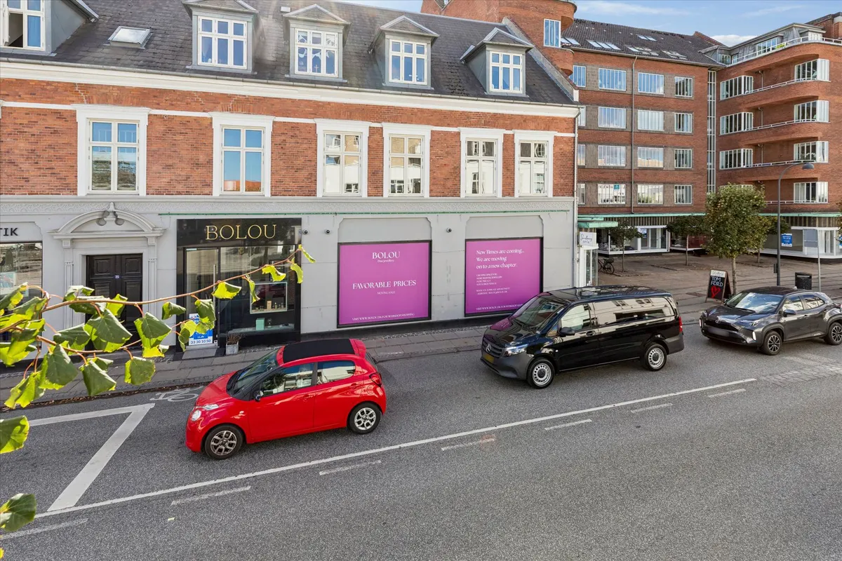 Butikslokaler med reklamebanner og parkerede biler på Jægersborg Allé, Gentofte.