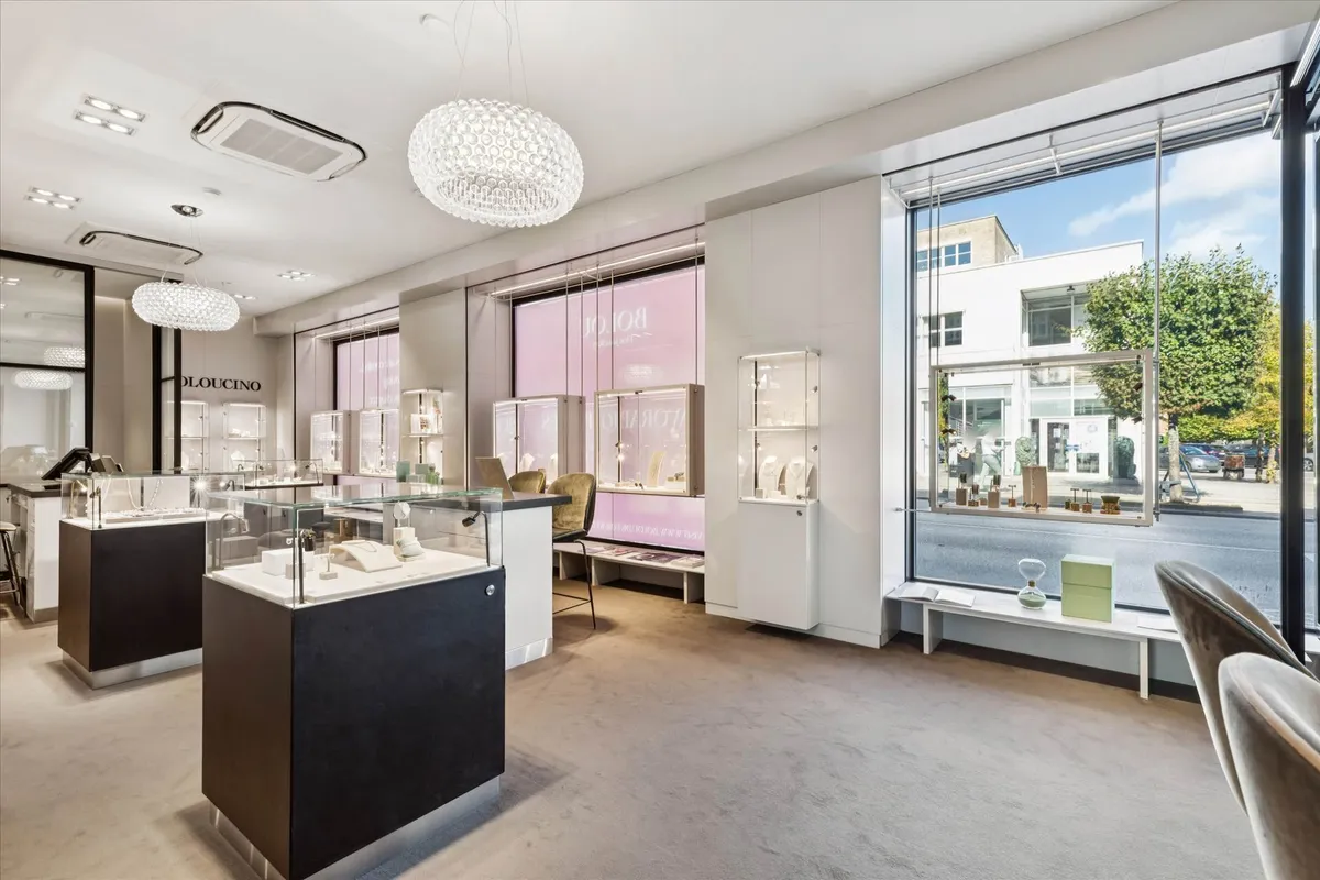 Butik med flere udstillingsvitriner med smykker og ure, lysekroner, og et stort vinduesparti med udsigt til en gade med