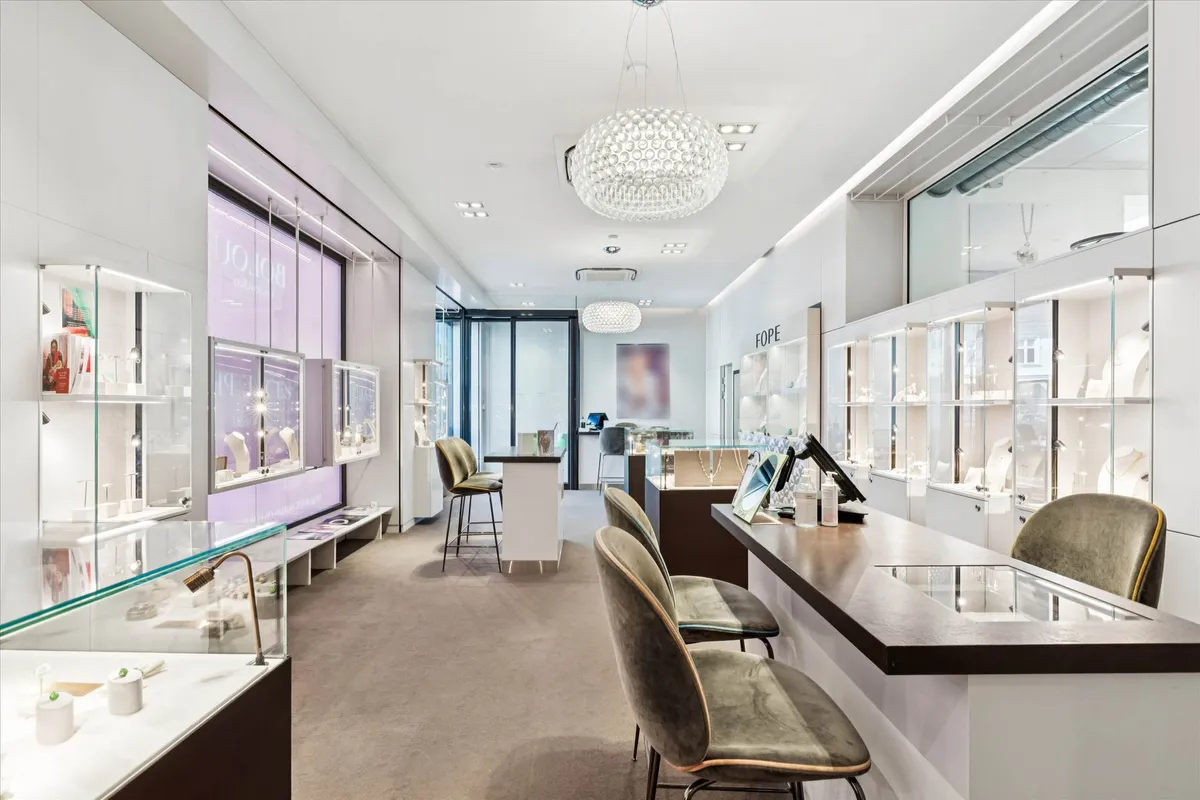 Showroom med gulv til gulv glasvinduer og store lysekroner, forskellige smykkeskabe, og to smykkesælgere i et salgsrum