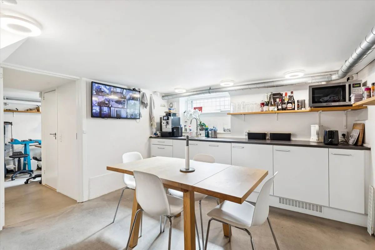 Et køkken med hvidt bord og stole, køkkenapparater og en tv-skærm med kameraoptagelser.