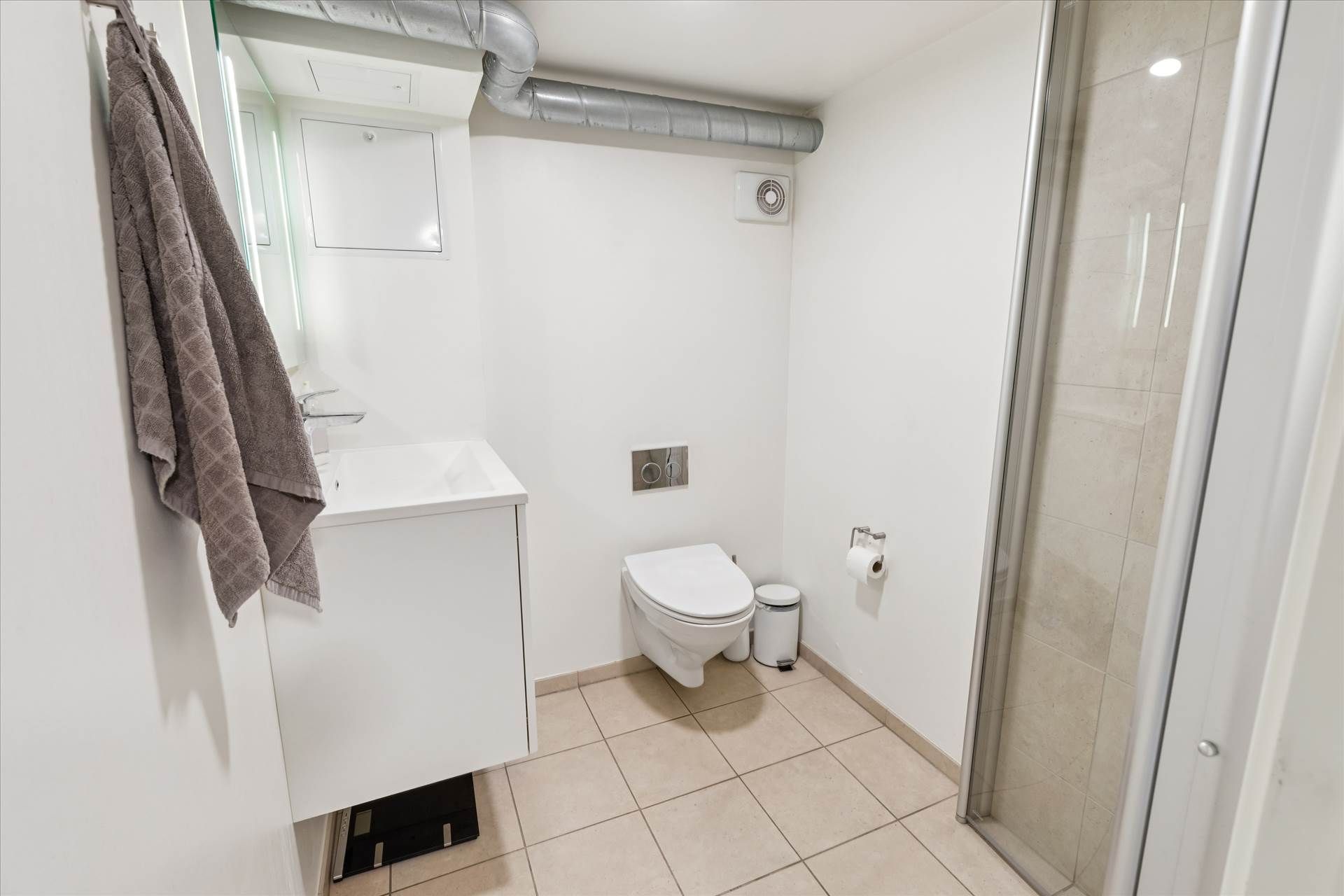 Ren og moderne badeværelse med hvidt badekar, ren hvid toilet, ren hvid vask og hvidt toiletpapirhylde.