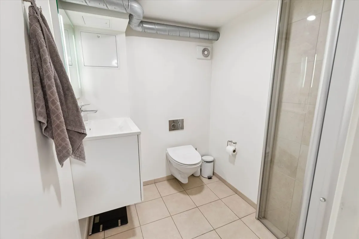 Ren og moderne badeværelse med hvidt badekar, ren hvid toilet, ren hvid vask og hvidt toiletpapirhylde.