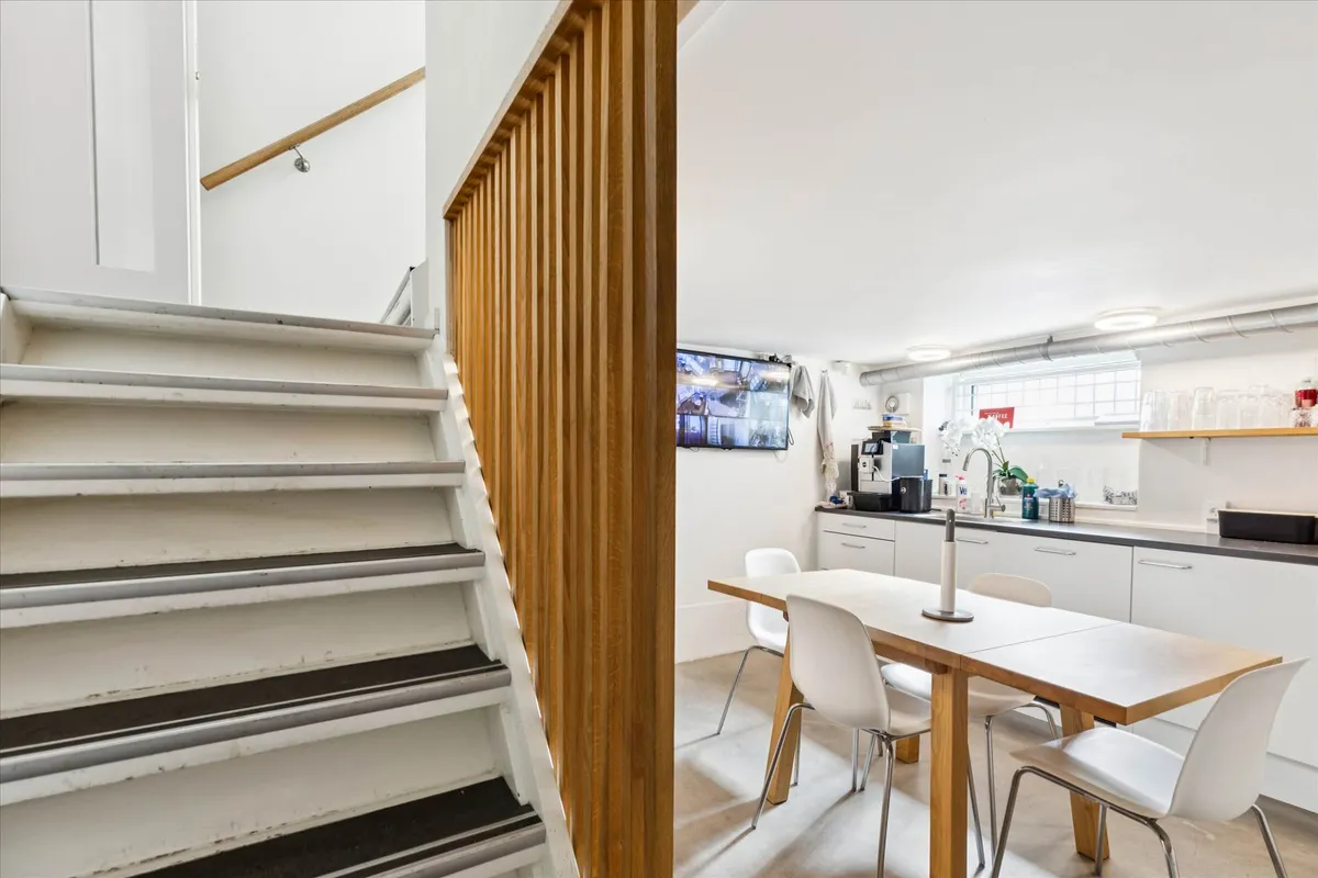 En moderne køkkendel med hvide møbler og lysegulv samt et træbord med fire hvide stole