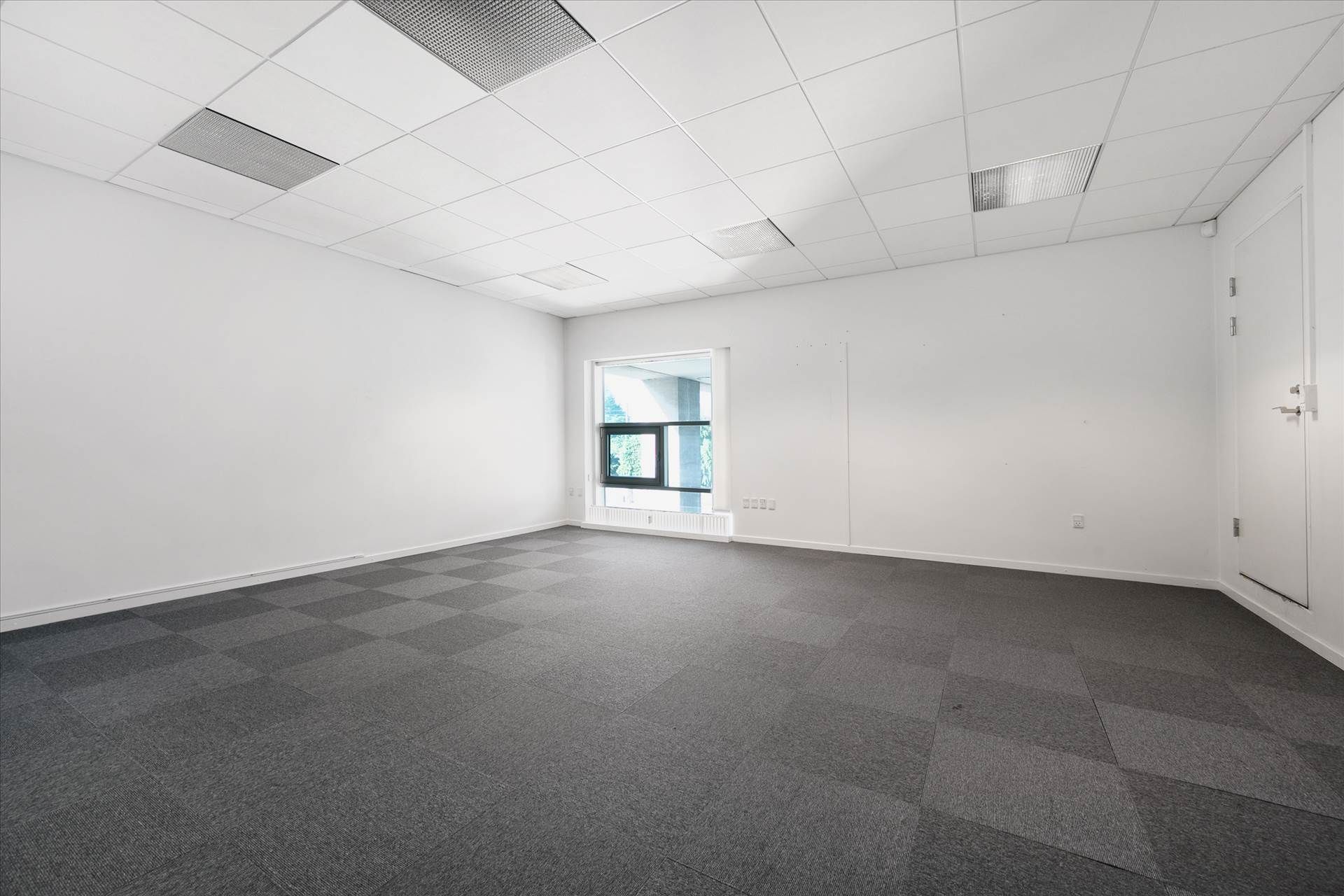 Det er en moderne kontorrum med hvide vægge, et gråt gulv og hvide loftsplader med indbygget ventilation
