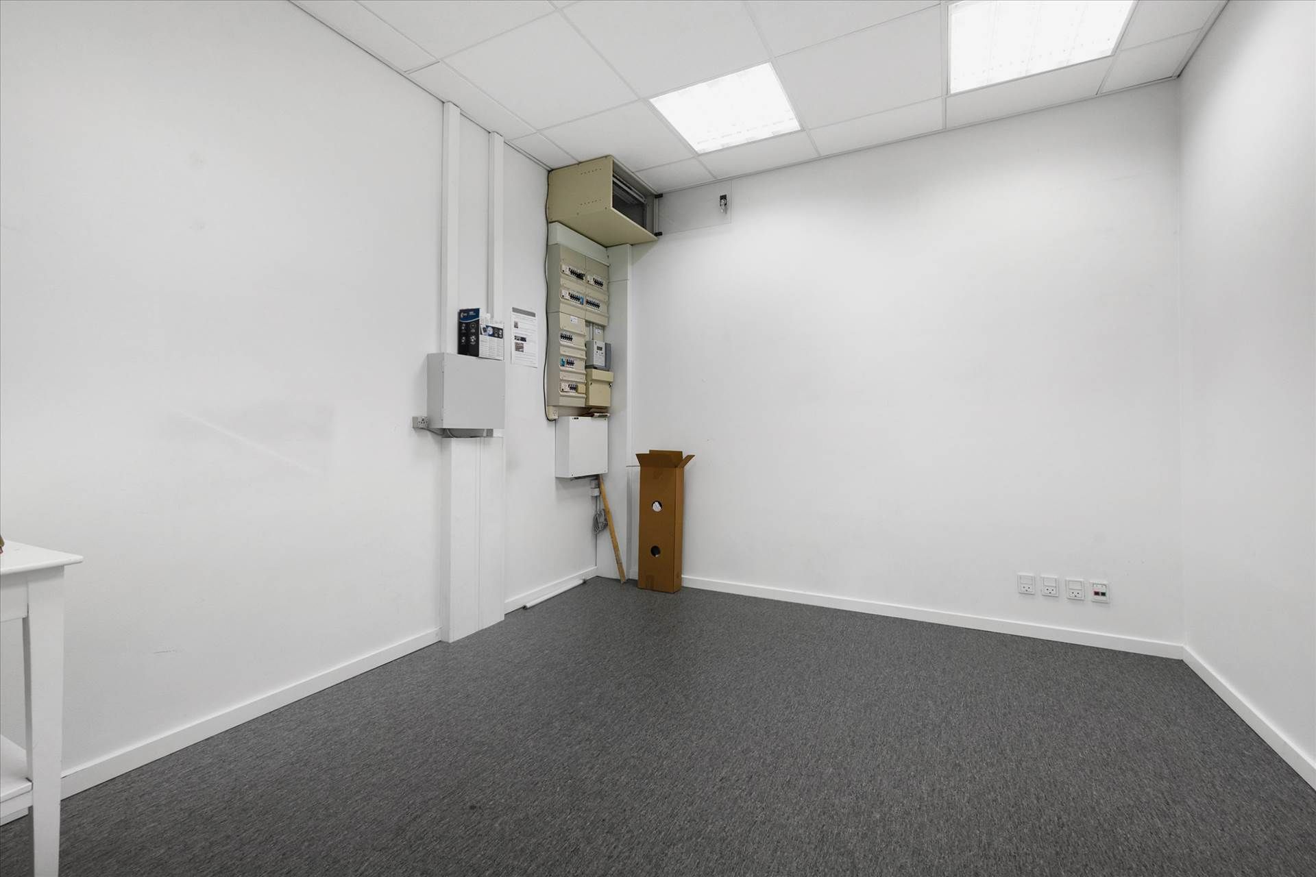 Tomt kontor med hvide vægge, gulv og loft, sammen med et træhylde og en hvid bordkant og tre stikkontakter i væggen