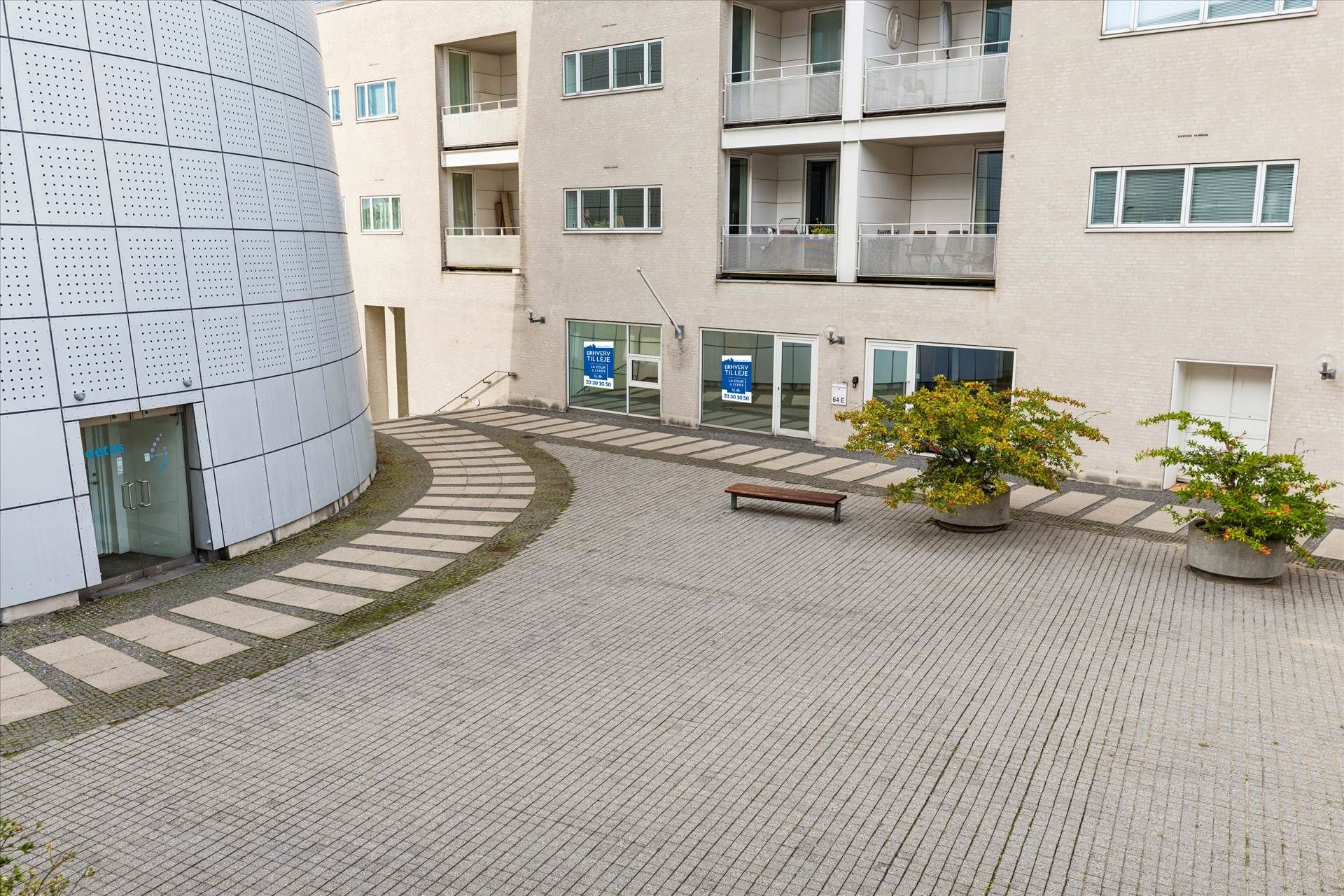 Kontorbyggeri med tæt beplantede arealer, et træklatret beklædningspanel og to lyserøde skilte på hoveddøren