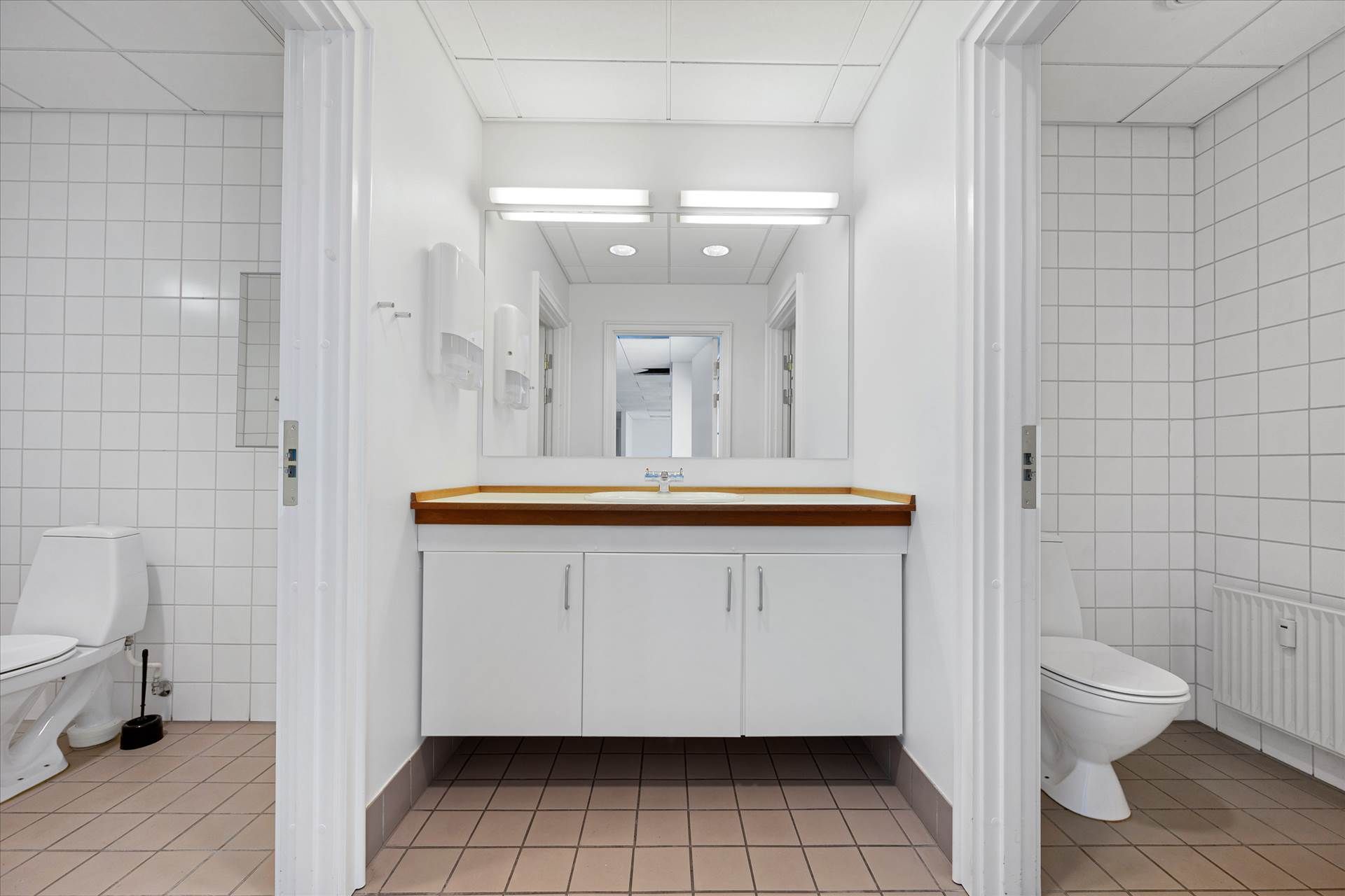En hvid toiletrum med toilet, håndvask, og spejl i et rum med kakelede vægge og gulv