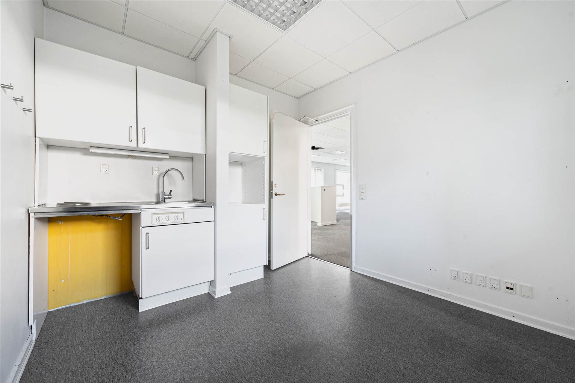 En minimalistisk køkken med hvide vægge, hvidt loft, hvide skabe og højt kvalitetsgulv. Et rustfrit stål vaskebækken med