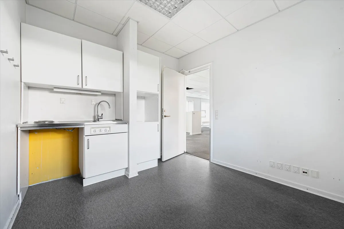 En minimalistisk køkken med hvide vægge, hvidt loft, hvide skabe og højt kvalitetsgulv. Et rustfrit stål vaskebækken med