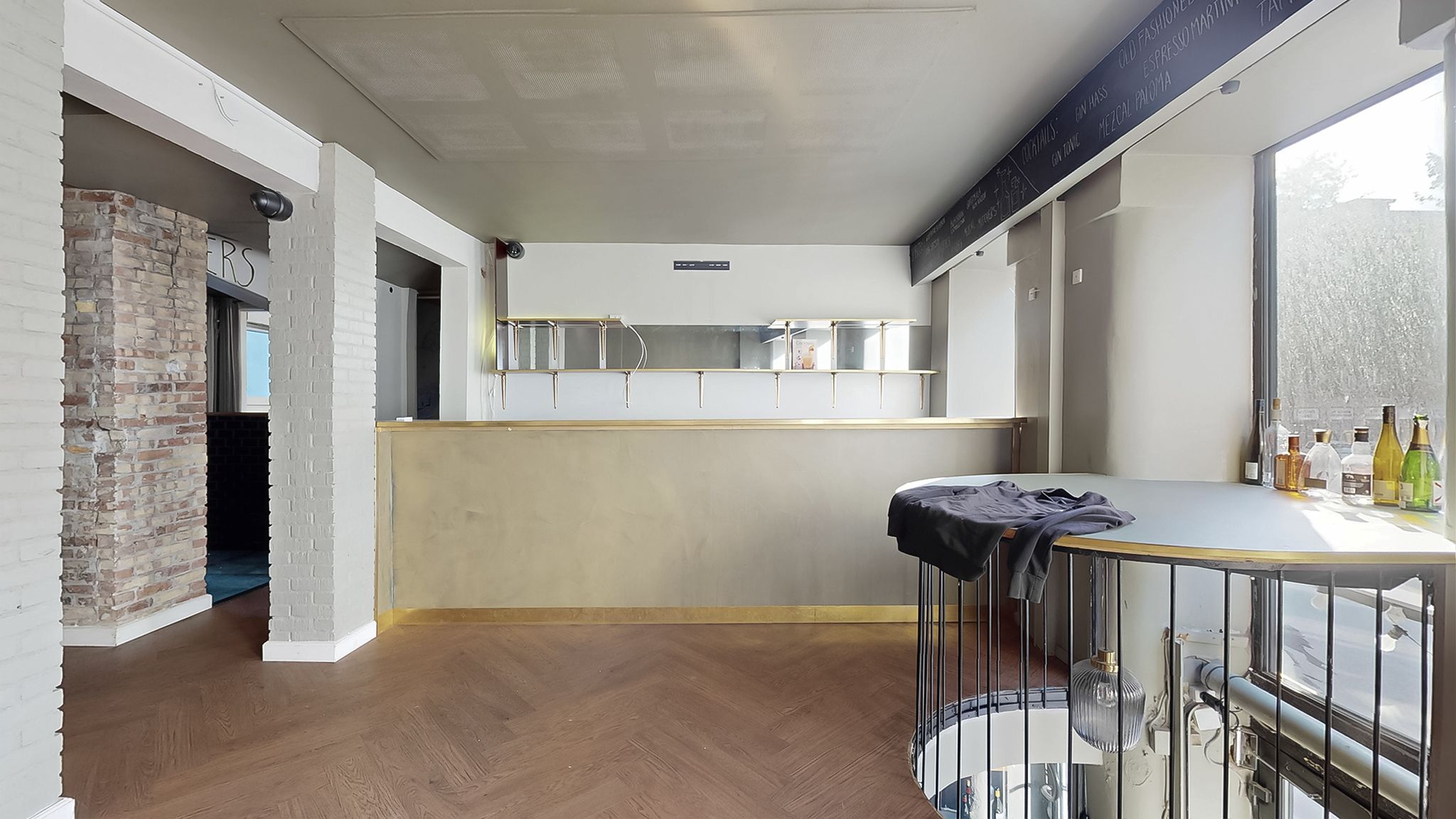 En hyggeligt indrettet bar med åben køkkendel, hvor der er flasker og glas samt en udsigt til en spiraltrappe