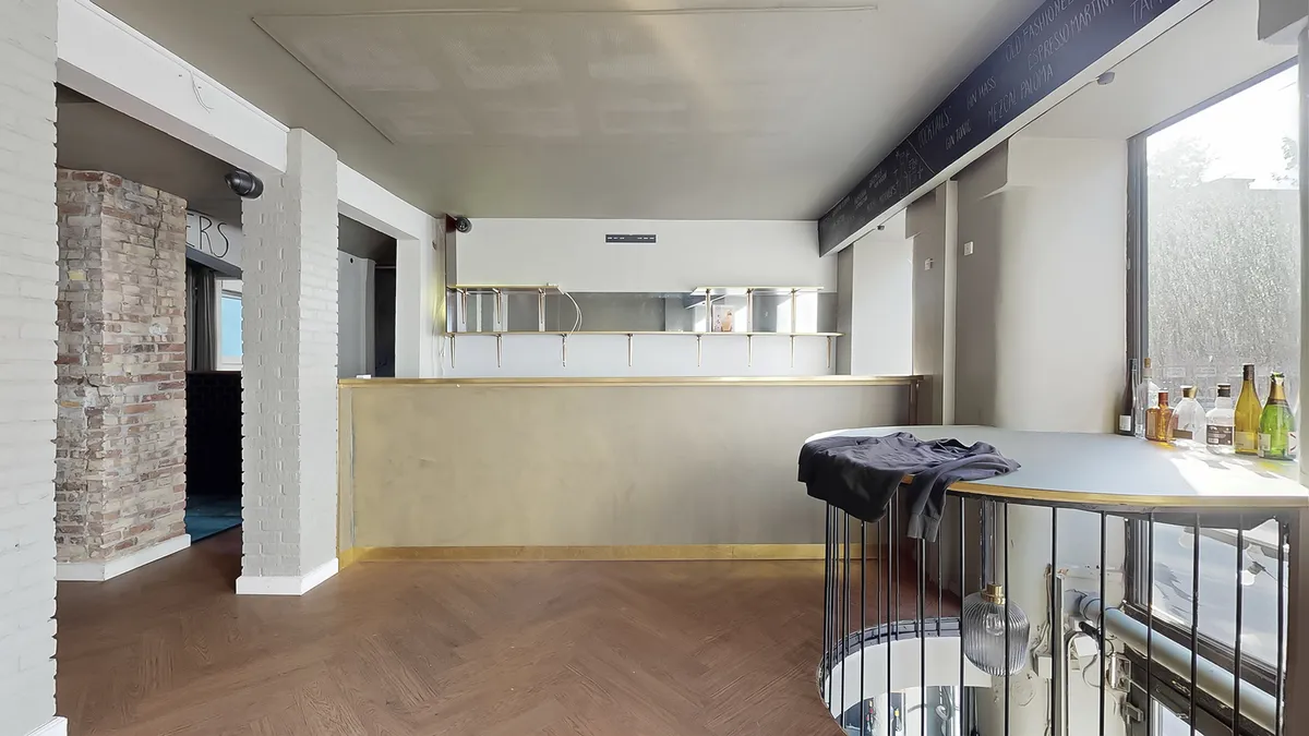 En hyggeligt indrettet bar med åben køkkendel, hvor der er flasker og glas samt en udsigt til en spiraltrappe