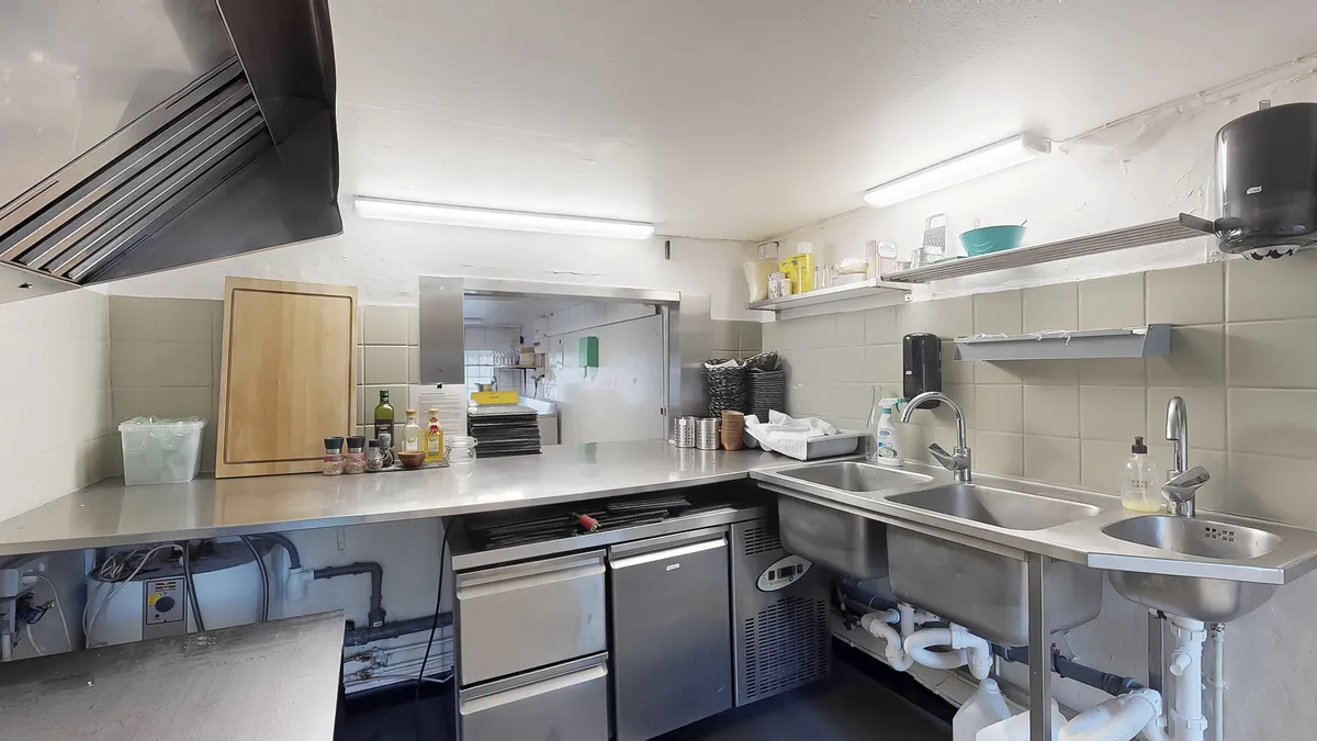 En ren og moderne køkkenfacilitet med to dybe vaskebassiner, hånddesinfektionsmiddelflaske, håndklæder og køkkenredskaber,