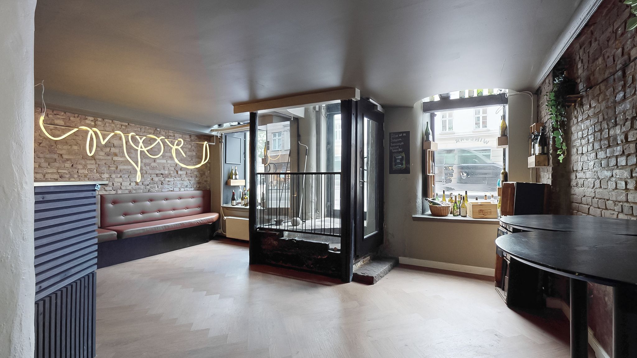 Et moderne indre lokale med to runde borde, et lædersofa, gulvbelægning og lyse neonlyse.