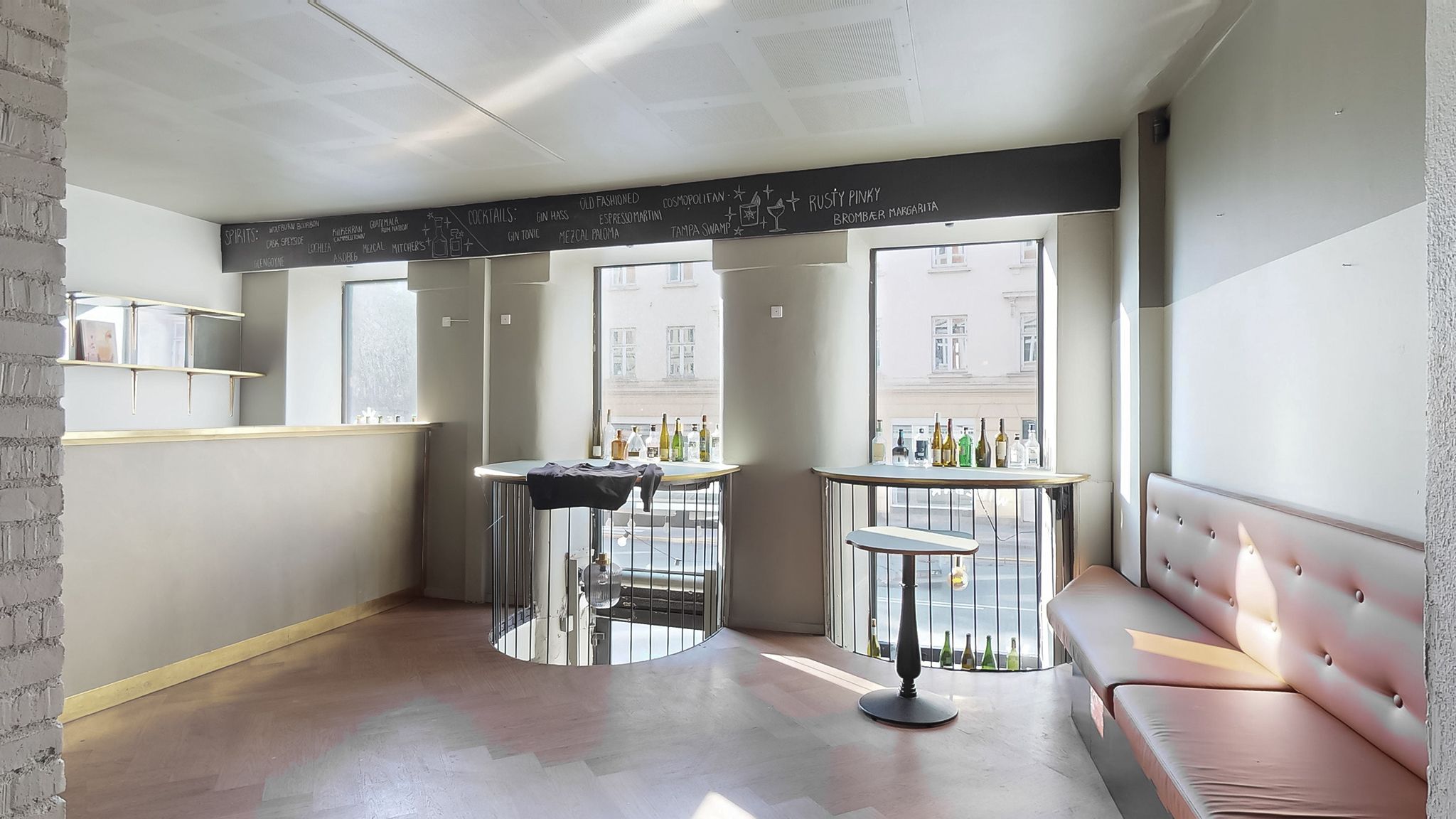 Elegant indretning med vinflasker og stolpeborde, og en menu med cocktails og spiritus i et café- eller barmiljø