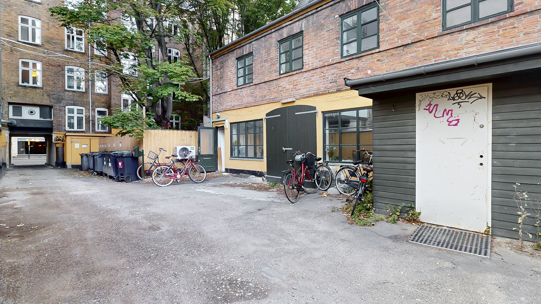Flere cykler parkeret ved gulvet, stående ved siden af gamle bygninger med flere vinduer og et gult loft