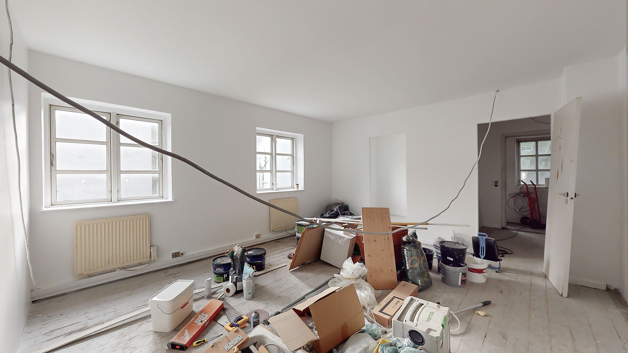 Rum med hul loft, jordnære vinduer og forskellige værktøjer og materialer som maling, søjler og kasser fordelt rundt i