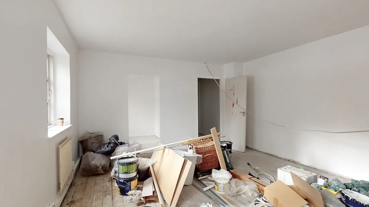 Tomt lokale med hvide vægge, højloft, trægulv og en åben dør med røde prikker på hvidt dørblad