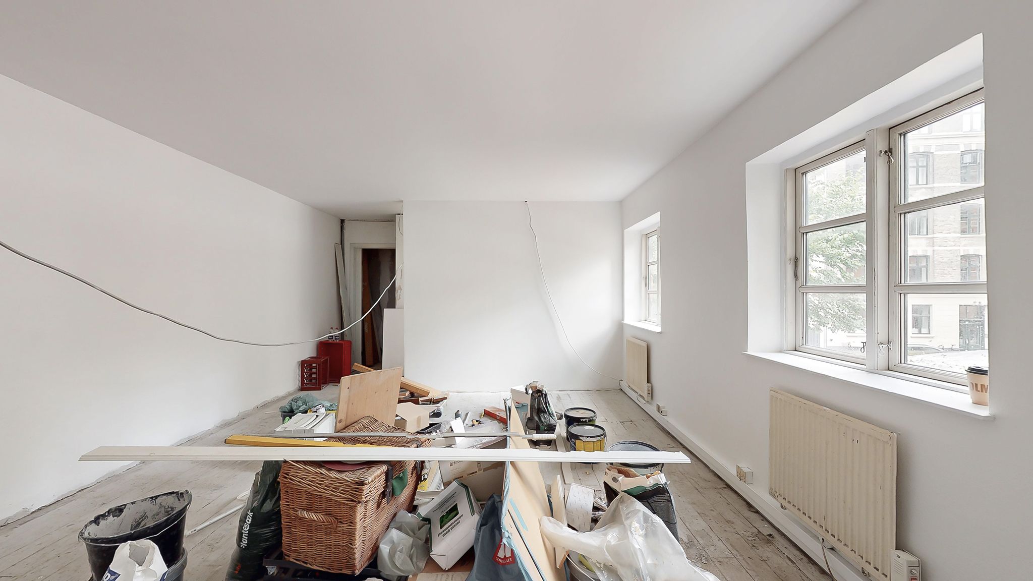 Et rum med to vinduer og en hvid væg, hvor der er opbevaret diverse genstande og værktøj