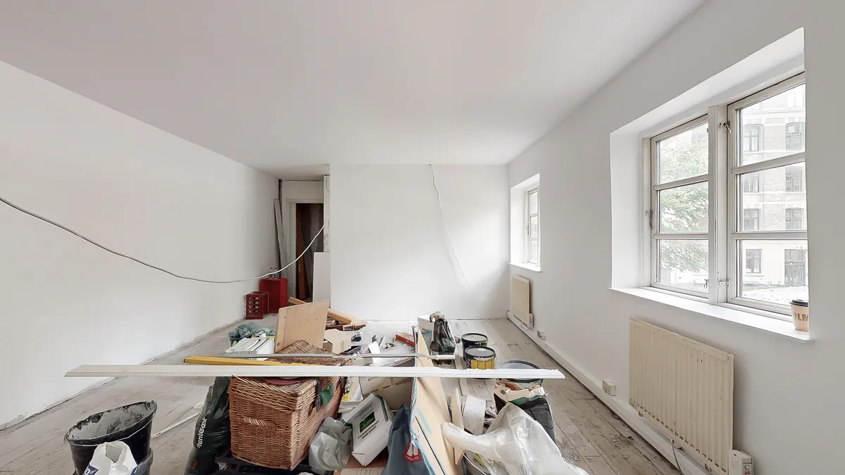 Et rum med to vinduer og en hvid væg, hvor der er opbevaret diverse genstande og værktøj