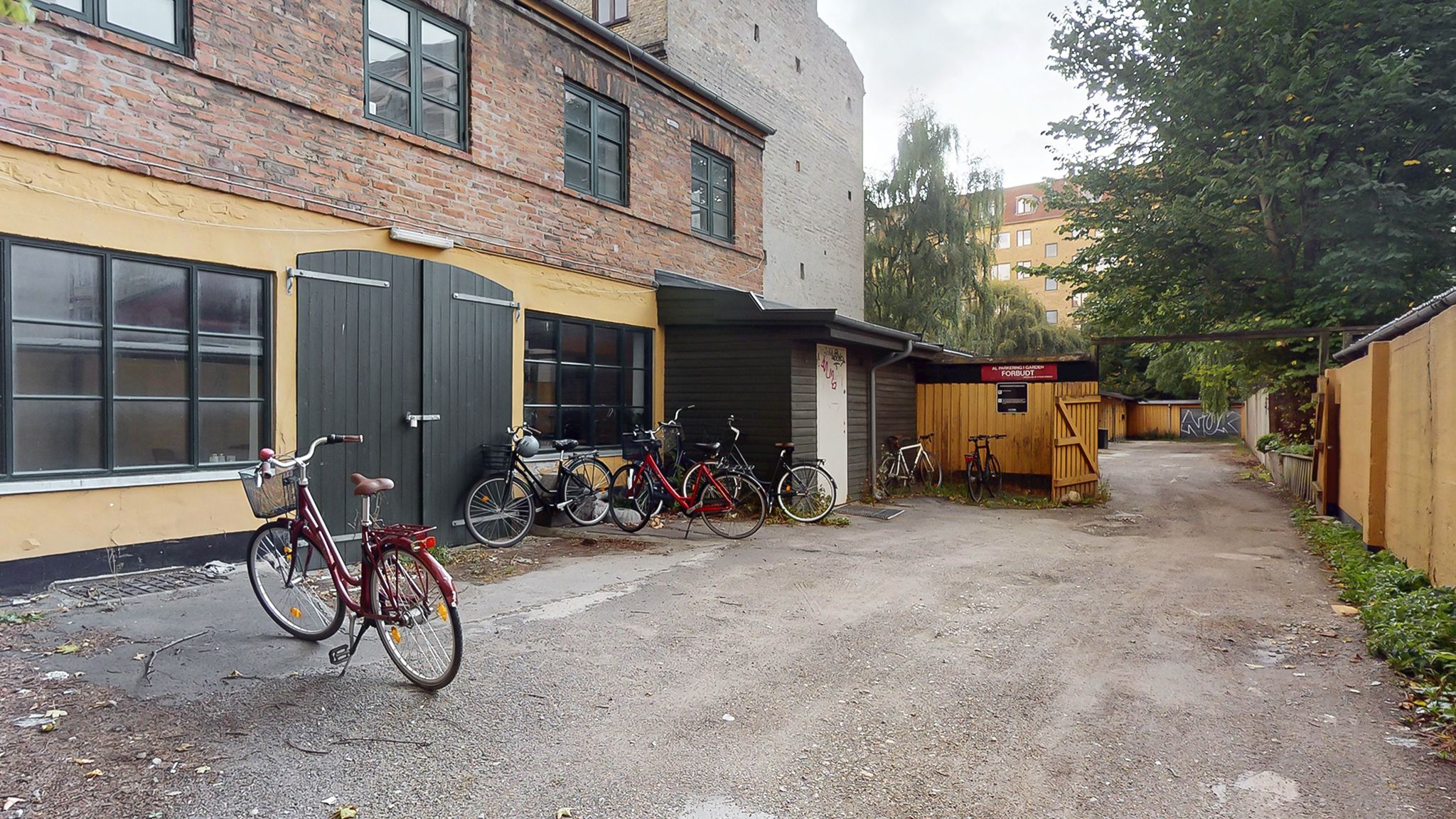 Flere cykler parkeret udenfor en bygning med en åben garagedør og en skilt med tekst