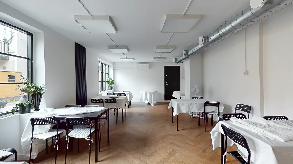 Elegant indrettet kontor med hvide vægge, lyse loftsplader og trægulve. Fire borde med hvide klud og stolpeformet stol.