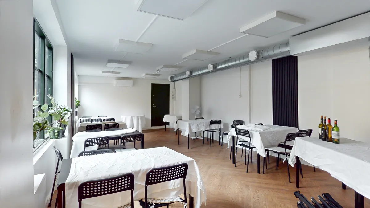En tom konferencelokale med hvide borde og stole, vinflasker på bordene og et klimaanlæg i væggen
