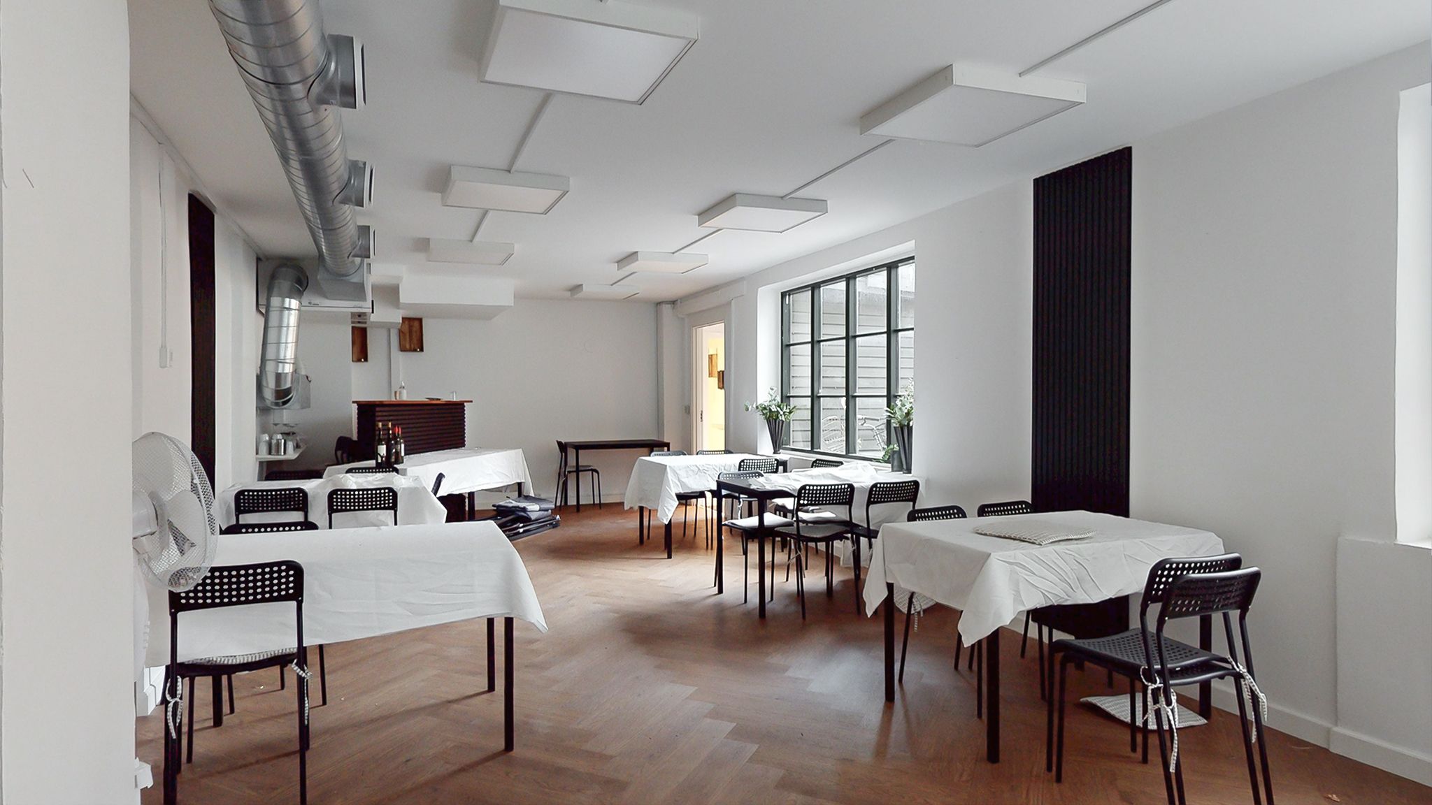 Et moderne mødelokale med hvide vægge og loft, trægulv, og borde og stole dækket i hvide klud. De lyse loftslamper og