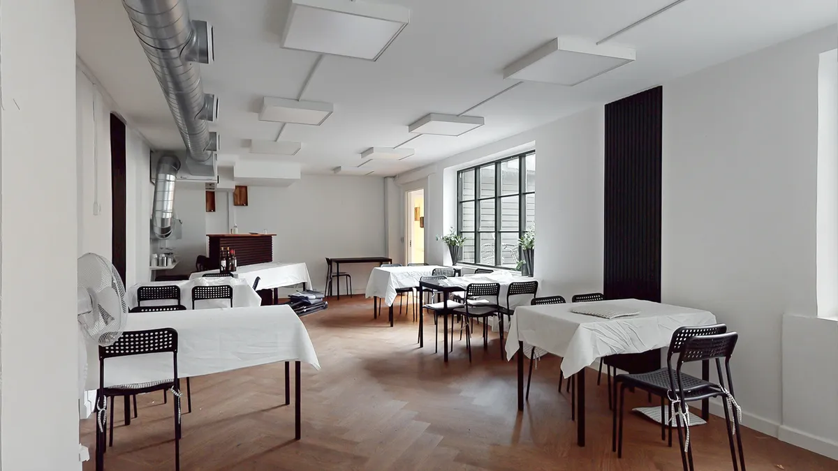 Et moderne mødelokale med hvide vægge og loft, trægulv, og borde og stole dækket i hvide klud. De lyse loftslamper og