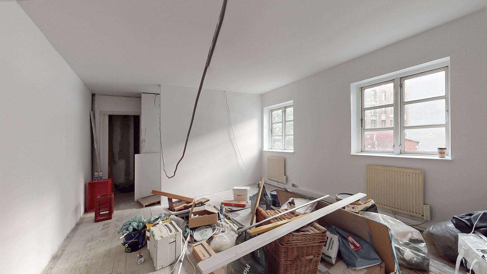 Rum med hvide vægge, loft og gulv samt flere genstande, kartoner og en kaffekop på vindueskarm